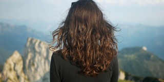 长头发的徒步旅行者女孩在奥地利萨尔兹卡默古特的沙夫伯格山观看史诗般的景色。60帧/秒的慢速镜头，在阿尔卑斯山的山峰上吹着风。