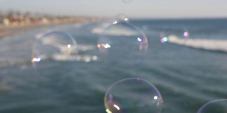 在加利福尼亚的海滨码头上吹着肥皂泡，模糊了夏日的背景。创造性的浪漫隐喻，梦想幸福和魔力的概念。抽象象征童年、幻想、自由