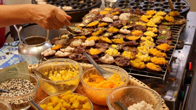 异国情调的东方美味甜点，不同寻常的色彩斑斓的传统菜肴在柜台上的集市与街头小吃。曼谷的晚间美食广场，烹饪之都。夜市。
