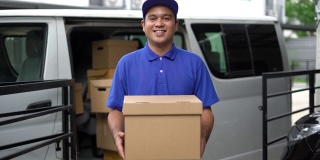 电晕病毒概念，Smiley蓝色英俊的亚洲男子拿着包裹纸箱站在货车前面。4k分辨率和慢动作拍摄。