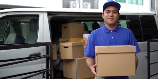 电晕病毒概念，Smiley蓝色英俊的亚洲男子拿着包裹纸箱站在货车前面。4k分辨率和慢动作拍摄。