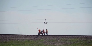 三名铁路工人在轨道上搬运手推车，以探索轨道，防止事故发生