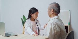 泰国可爱的女孩玩是医生检查一个老男人病人使用听诊器在家