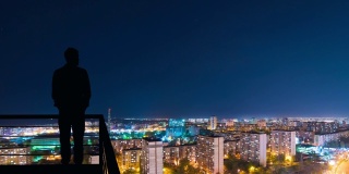 在城市夜景背景下，站在建筑物顶端的男子