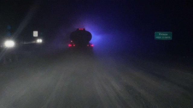 车辆视点拍摄在暴风雪中，在繁忙的道路上驾驶在一辆油罐车的后面，而前方的应急灯在夜晚闪烁