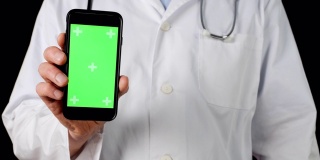 医生的手显示手机与绿色色键屏幕近处，孤立的黑色背景。男医生手持智能手机与绿色屏幕前摄像头近距离