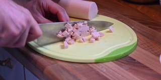 用一把锋利的刀子在厨房架子上的厨房板上把香肠切成小块