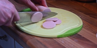 在厨房架子上的一块厨房板上，用锋利的刀子慢动作把香肠切成小块