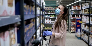 戴着防护面具和手套的年轻女子在超市选购意大利面。新冠肺炎疫情期间购物