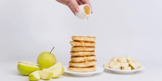 用香蕉、苹果、蜂蜜或枫糖浆制作的甜煎饼的定格动画，在白色的背景上，特写。早餐、零食和适当营养的概念