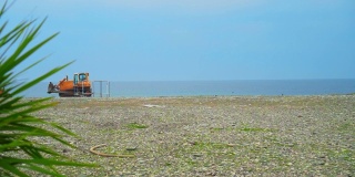 黄色的推土机骑在卵石滩上，填海造地。海滩景观