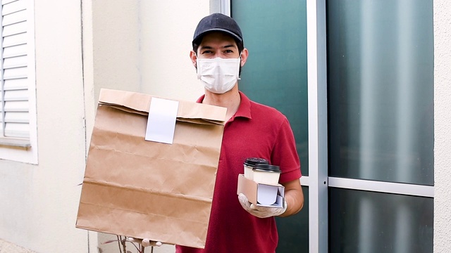 戴着口罩和手套的送货员站在住宅前。食品配送、杂货和用品的概念