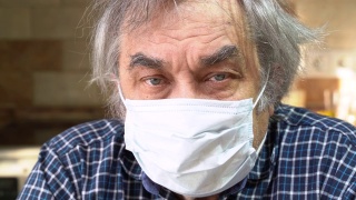 防病毒保护。新型冠状病毒肺炎那位戴着医用防护面罩的老人正坐在厨房的一张桌子旁。视频素材模板下载