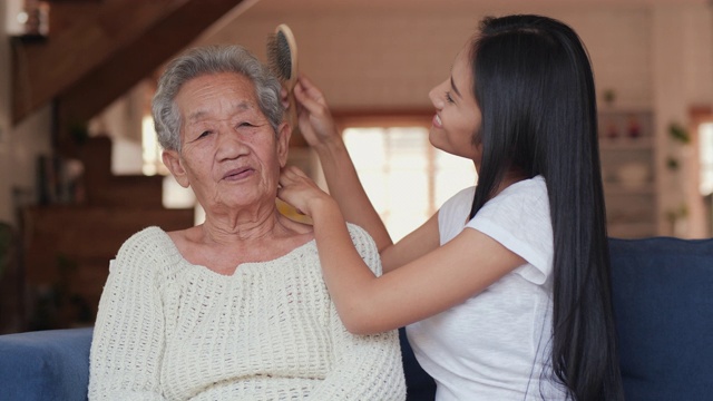 年轻妇女在家照顾她的母亲。她在客厅给她妈妈梳头。生活方式和保健概念。