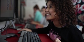 快乐的女学生坐在桌子上使用电脑在电脑课上在私立学校