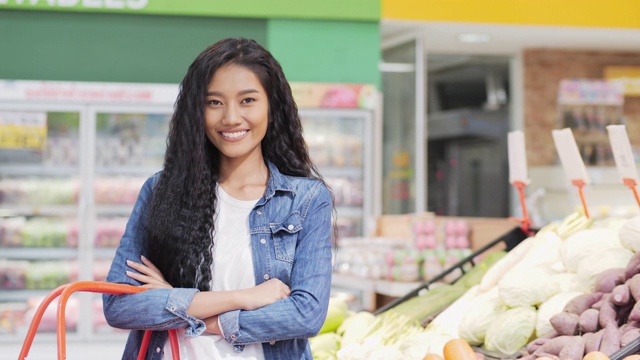 肖像美丽的女人看着相机微笑。年轻的亚洲女人站在超市，心情愉快。