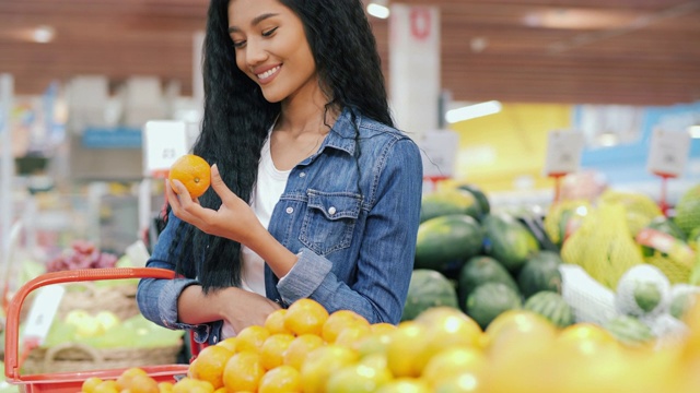 美丽的女人选择新鲜的橙子在杂货店购物。购买者选择一个柑橘并收集在袋子里。购物，买家和生活方式的概念。