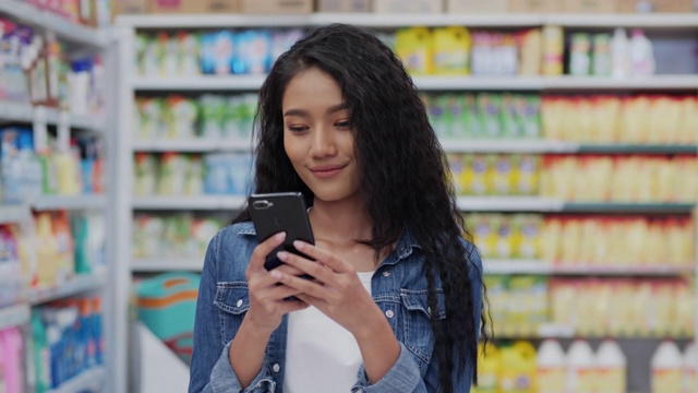 美女在超市用智能手机微笑研究产品细节。购物，客户，技术和生活理念。