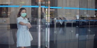 一个亚洲女人端着一杯咖啡打开门，走出办公大楼，慢镜头