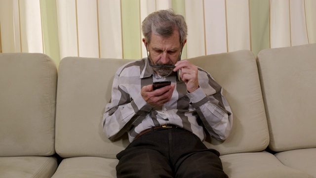 特写镜头。戴着眼镜的退休男性，正在打电话。退休老人在室内使用智能手机。现代科技，生活方式，衰老，残疾。