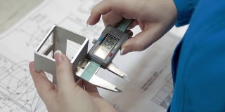 穿着长袍的工程师手握电子卡尺测量未来设备金属部分的宽度。电子卡尺显示器上的数字。