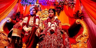 年轻的印度新婚夫妇坐在婚礼台上的豪华沙发上
