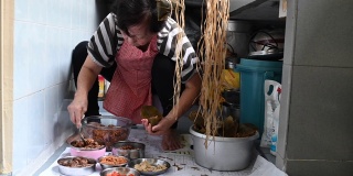 一位年长的亚洲华人妇女在她的厨房里准备粽子，把配料包好，为端午节做准备