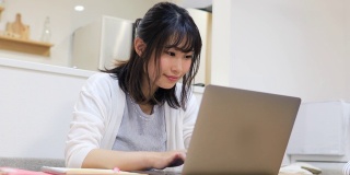 年轻女子在家工作，在笔记本电脑上输入信息
