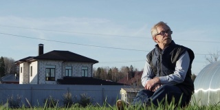 一位戴眼镜的老人低低地坐在绿色草地上的长凳上。