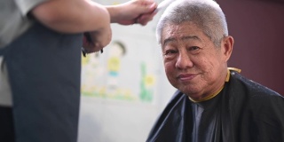 由于旅行禁令，一位亚洲华人中年妇女正在厨房里为她的父亲修剪头发