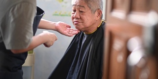由于旅行禁令，一位亚洲华人中年妇女正在厨房里为她的父亲修剪头发