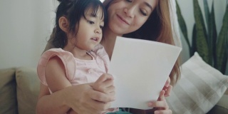一个年轻的女人和她的小女孩在家里看明信片。