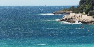 风帆冲浪者疾驰而过，海浪冲击着碧蓝海岸的岩石海岸，溅起水花，风景如画的堤岸，碧蓝的海水，著名的地方