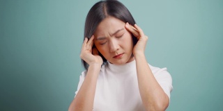 一名亚洲女性患有头痛偏头痛，孤立地站在蓝色背景上。卫生保健的概念。4 k的视频。