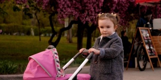 一个小女孩在公园里的花树旁玩婴儿车。