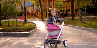操场上的公园里，一个小女孩推着一辆婴儿车在她前面。