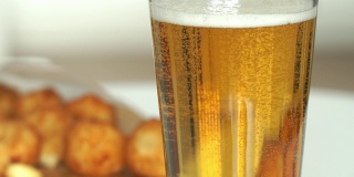 泡沫和啤酒泡沫的特写。Сold新鲜的啤酒倒进玻璃杯，背景是面包屑奶酪球。食物和饮料的背景。