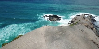 一架无人机拍摄到一对夫妇站在悬崖边欣赏风景。俯瞰印尼龙目岛丹戎安海滩。绿松石色的水。幸福和和睦
