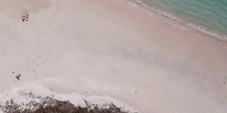 一对夫妇躺在印度尼西亚龙目岛粉红色海滩的沙滩上玩无人机。波浪轻轻地拍打着海岸。他们晒黑。快乐和粗心的时刻。