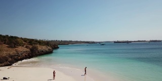 一对情侣在龙目岛的粉色沙滩上散步。这个地方是一块隐藏的宝石，不会被游客破坏。孤独和平静的感觉，海浪轻轻在沙滩上蔓延。色彩斑斓的悬崖