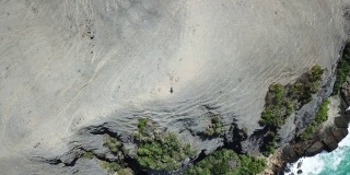 一对夫妇站在悬崖上，欣赏着印尼龙目岛丹戎安海滩的风景。贫瘠的悬崖。绿松石色的水。无人机飞得很高