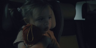 黄昏时分，一个小女孩独自坐在车里，抱着洋娃娃