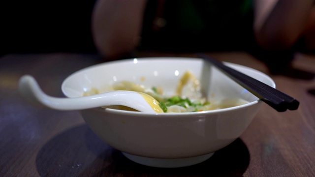 在一家亚洲餐馆里，母亲和孩子用筷子吃饺子。味道很辣。