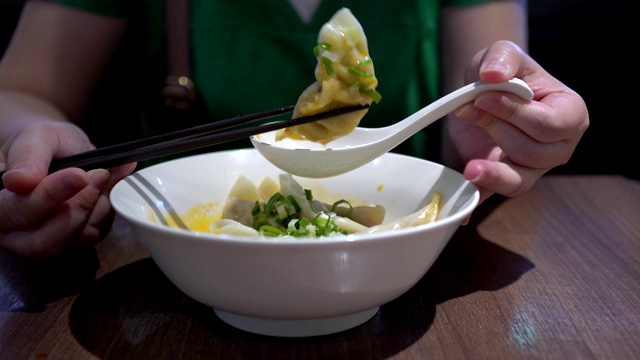在一家亚洲餐馆里，母亲和孩子用筷子吃饺子。味道很辣。