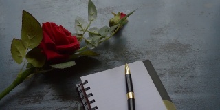 空白页笔记本，钢笔和美丽的红玫瑰在乡村金属地板背景与复制空间。情书写作建议或提议概念为情人节婚礼和假期。前视图。