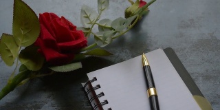 空白页笔记本，钢笔和美丽的红玫瑰在乡村金属地板背景与复制空间。情书写作建议或提议概念为情人节婚礼和假期。前视图。