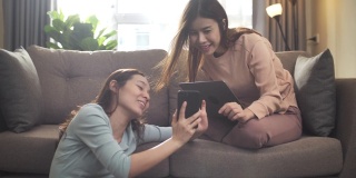 两个年轻的亚洲女性朋友坐在沙发上，用她的手机在家里