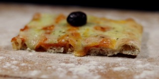 平面包披萨由奶酪和黑橄榄在砧板上与面粉在黑色的背景缓慢旋转