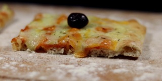 平面包披萨由奶酪和黑橄榄在砧板上与面粉在黑色的背景缓慢旋转