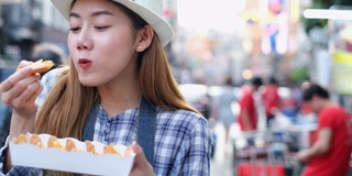 亚洲年轻女子在曼谷市集吃传统的亚洲街头食物。漂亮女人吃泰国街头小吃的特写。